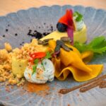 Delicately presented gourmet dish with vibrant colors and artistic flair on a textured plate.