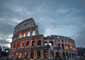 The Colosseum in Rome is beautifully illuminated against a dramatic evening sky, showcasing its ancient Roman architecture.